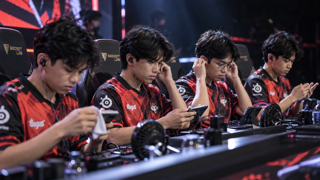 Mulai Besok, Bigetron dan Alter Ego Berebut Tiket Grand Final PMGO S2: Jadwal, Format, dan Peluang 2026 7 Empat pemain dengan seragam merah hitam bersiap mengatur perangkat ponsel dan earphone mereka di meja panggung sebelum pertandingan pertama.